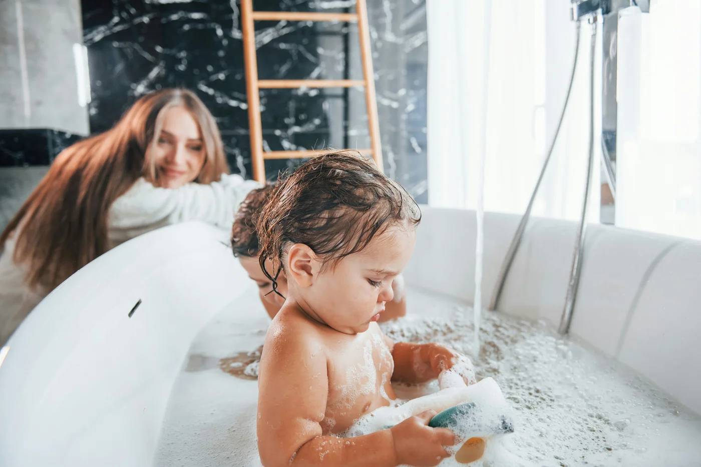 Child in a bubble bath with a caregiver nearby